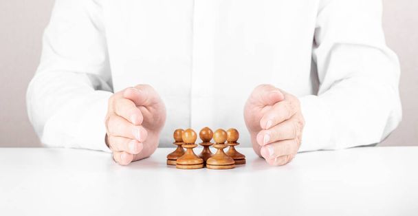 Zakenman die kleine schaakgroepen onder zijn handen redt. Begrip leiderschap, teamwork en verzekering - Foto, afbeelding