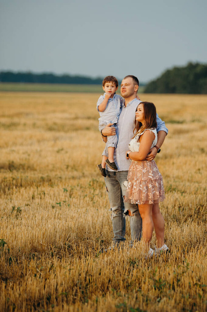 The concept of a happy family. Son with mom and daddy. Happy family in the field evening light of a sun. Mother, father and baby son happy walk at sunset, parents hold the baby.  - Photo, image