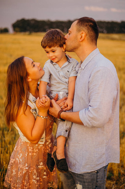 The concept of a happy family. Son with mom and daddy. Happy family in the field evening light of a sun. Mother, father and baby son happy walk at sunset, parents hold the baby.  - Foto, Bild