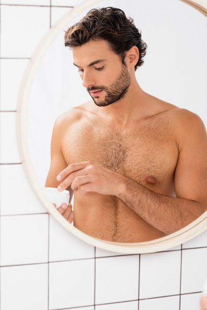 Shirtless man holding jar with cosmetic cream in bathroom  - Фото, зображення