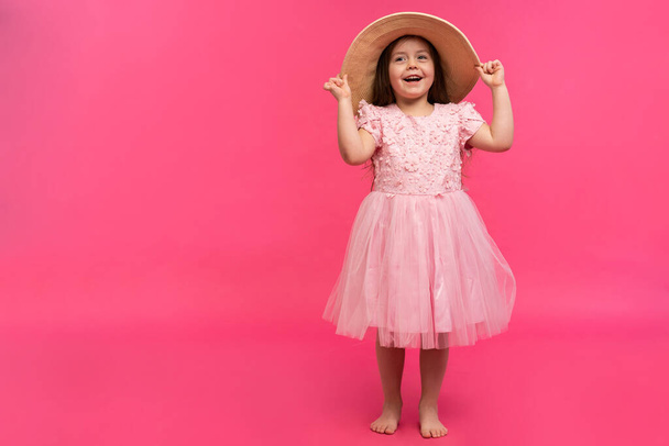 Portrait of cute little girl in straw hat and pink dress in the studio on pink background. Copy space for text. - Fotó, kép