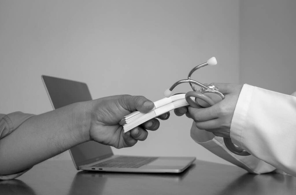 Black and white image of doctor's hand is receiving bundle of banknotes from anonymous man's hand at doctor office on corruption and bribe in medical health care concept - Photo, Image