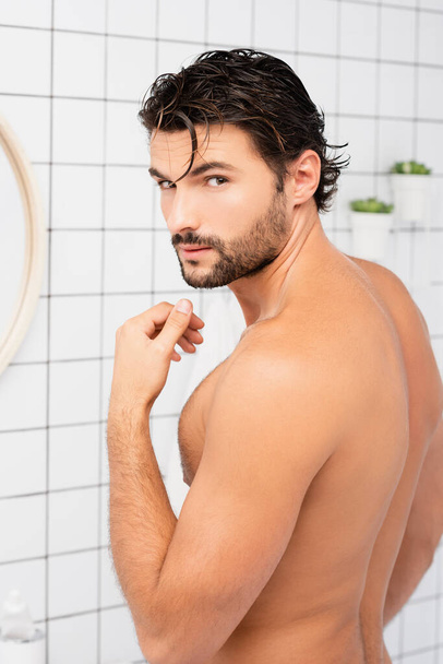 Hombre musculoso con el pelo mojado mirando a la cámara en el baño  - Foto, Imagen
