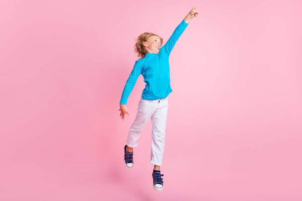 Full length photo of small boy jump raise fist wear blue turtleneck pants sneakers isolated pastel pink color background - Fotografie, Obrázek