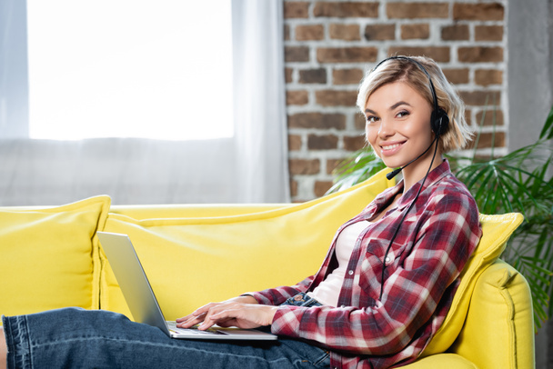 молодая блондинка с вебинаром и сидя на диване с ноутбуком - Фото, изображение