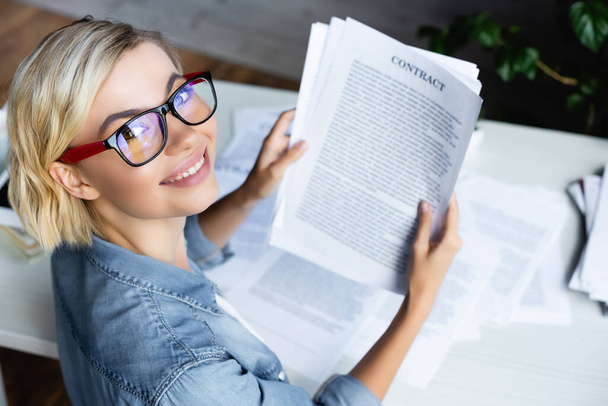 Hochwinkelaufnahme einer jungen blonden Frau mit Brille, die einen Vertrag hat - Foto, Bild