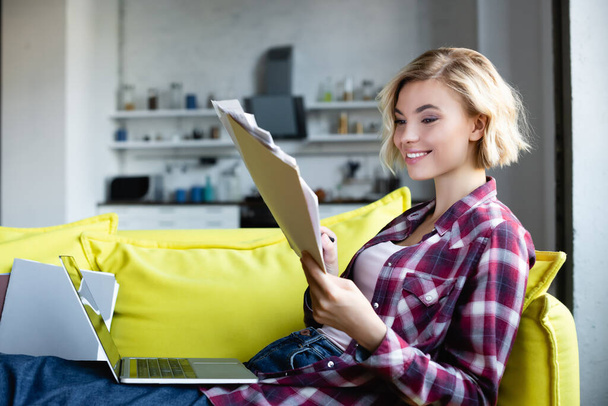 blonde woman in checkered shirt working from home and looking through documents - Photo, Image