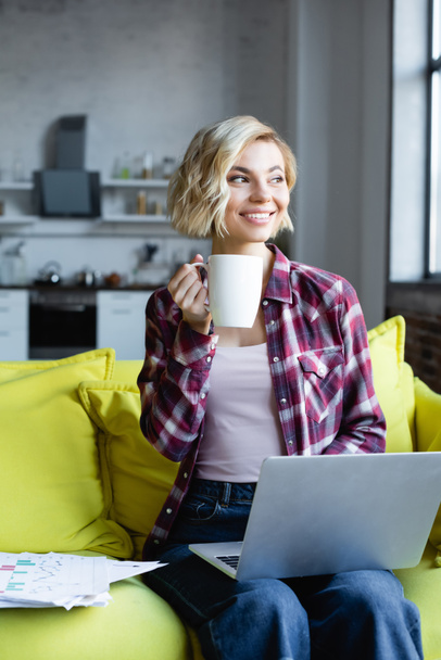 blonde woman in checkered shirt working from home and drinking tea - Photo, Image