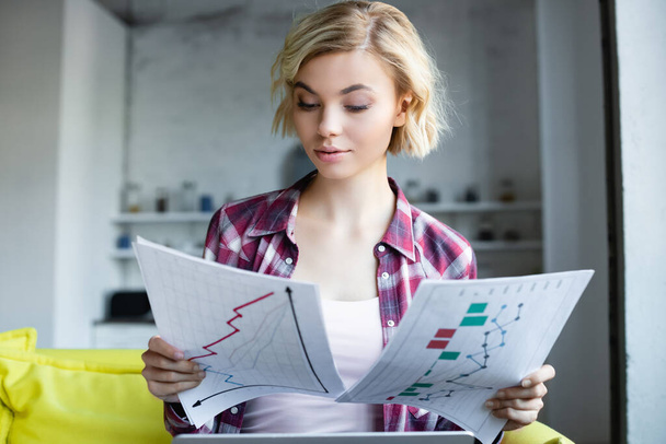 blonde woman in checkered shirt working from home and looking at graphs - Фото, зображення