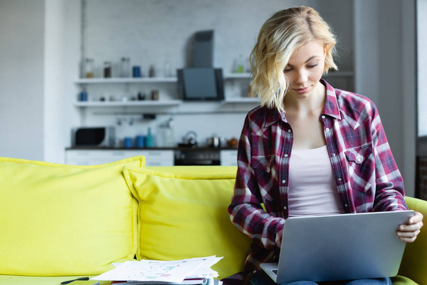 femme blonde en chemise à carreaux travaillant à la maison et tapant sur ordinateur portable - Photo, image