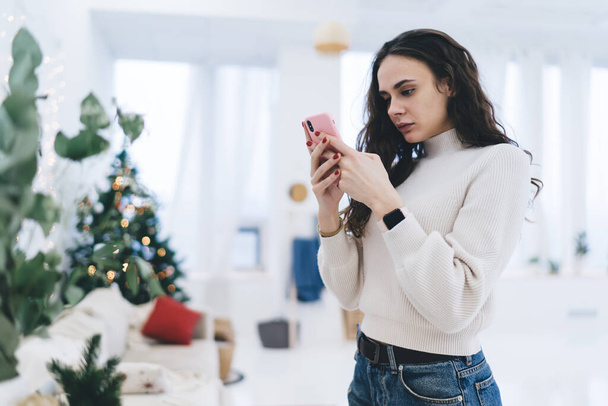 Brunette caucasian woman blogger standing with mobile phone checking mails and news from social networks, serious hipster girl influencer holding smartphone share media and multimedia content - Foto, imagen