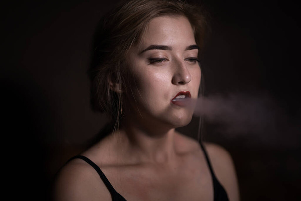 Bella ragazza con le labbra rosse soffia fumo da un narghilè dalla bocca - Foto, immagini