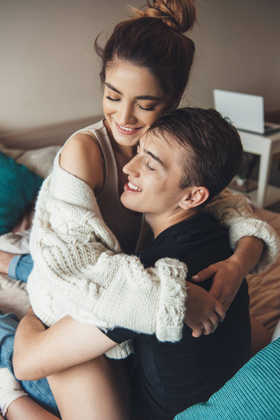 Mujer caucásica abrazada por su amante mientras jugaba en la cama temprano en la mañana en un suéter de punto sonriendo con los ojos cerrados - Foto, imagen