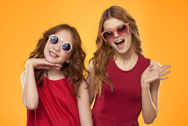 Счастливая женщина и маленькая девочка в красном платье веселятся на желтом фоне модных эмоций сестер весело Copy Space. - Фото, изображение