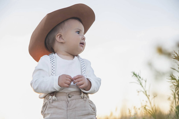 baby in een hoed en pak met bretels kijken in het veld - Foto, afbeelding