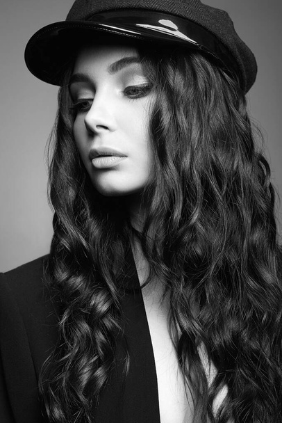 ασπρόμαυρο πορτραίτο του μοντέρνου όμορφου κοριτσιού στο καπέλο. Κομψό όμορφη νεαρή γυναίκα με υγιή σγουρά μαλλιά - Φωτογραφία, εικόνα