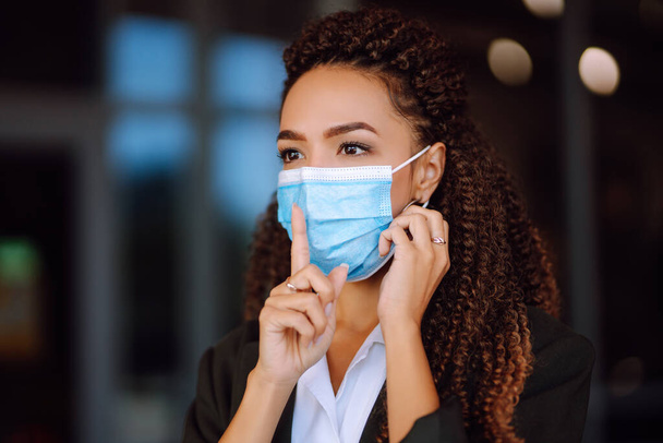 Young woman in protective sterile medical mask on her face shows a gesture: shh. silence. Businesswoman dressed in suit showing silence gesture in quarantine city. Covid-2019. - Photo, Image