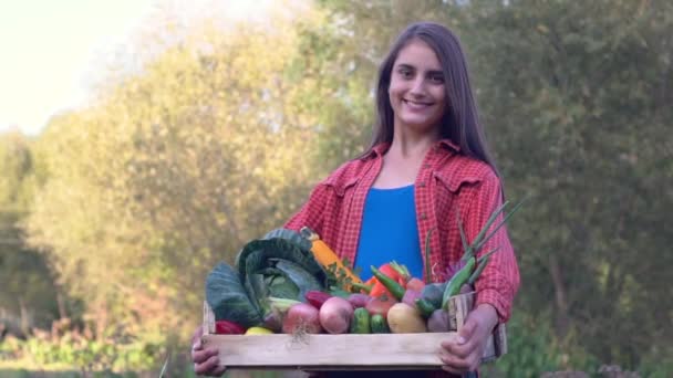 Agricoltore azienda scatola di legno piena di verdure sul campo biologico. Ritratto di donna caucasica sorridente in giardino. - Filmati, video