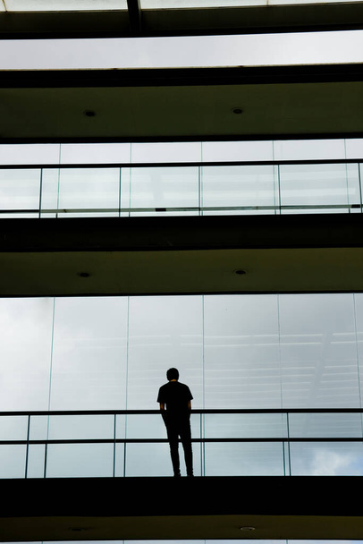 Vista de la silueta del joven empresario en un moderno edificio de oficinas interior con ventanas panorámicas. - Foto, Imagen
