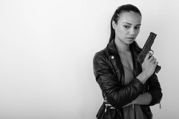 Studio shot of young beautiful Asian woman wearing leather jacket against white background in black and white - Fotoğraf, Görsel