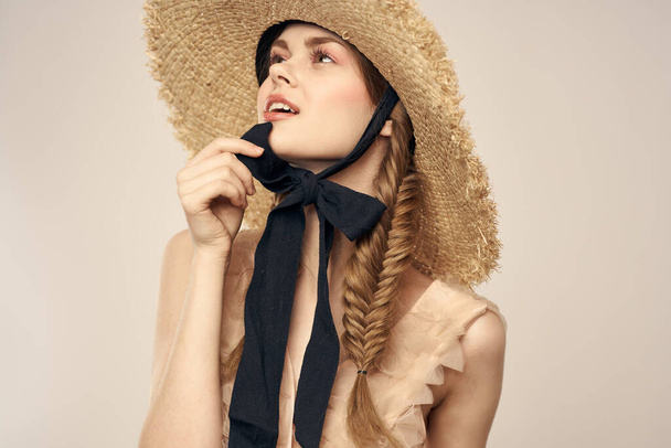милая девушка в соломенной шляпе с черной лентой и платье на бежевом фоне обрезанный вид - Фото, изображение