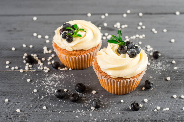 Creamy cupcakes with blueberries on the wooden background - Фото, изображение
