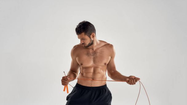 Healthy and active lifestyle. Young athletic man in sportswear holding skipping rope while standing isolated over grey background - Foto, imagen