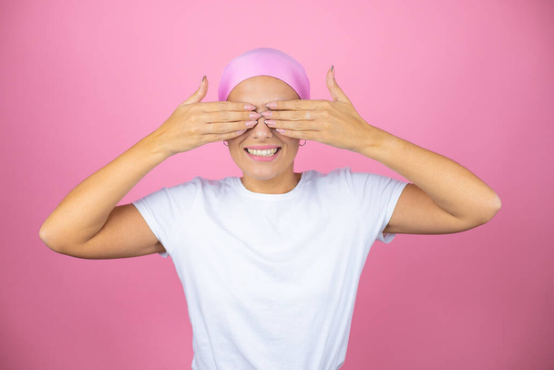 Young beautiful woman wearing pink headscarf over isolated pink background covering eyes with hands smiling cheerful and funny. Blind concept. - Фото, зображення