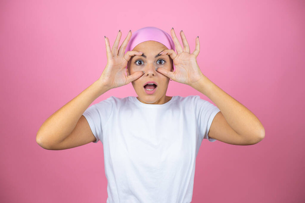 Young beautiful woman wearing pink headscarf over isolated pink background Trying to open eyes with fingers, sleepy and tired for morning fatigue - Foto, Bild
