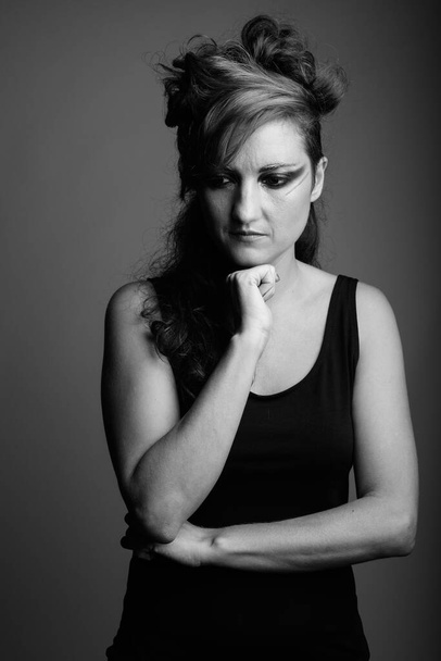 Estudio de mujer hermosa con el pelo atado y maquillaje contra fondo gris en blanco y negro - Foto, Imagen