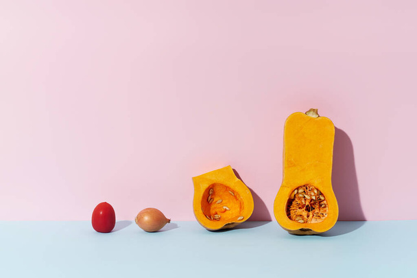 Halved butternut squash with tomato and onion on pink and blue background. Healthy vegetarian ingredient. - Foto, Imagen