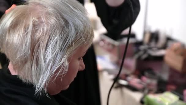 Oudere vrouw met kort grijs haar doet styling in een schoonheidssalon. Video - Video