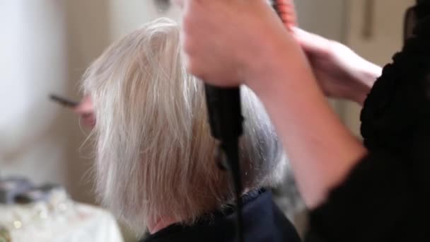 Oudere vrouw met kort grijs haar doet styling in een schoonheidssalon. Video - Video