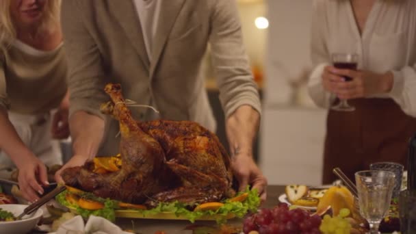 Slow motion shot of unrecognizable man finishing setting dining table for Thanksgiving celebration putting roasted turkey on it - Footage, Video