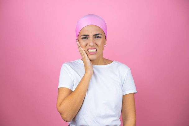 Молода красива жінка в рожевому хустці над ізольованим рожевим фоном торкається рота рукою з болючим вираженням через зубний біль або стоматологічні захворювання на зубах
 - Фото, зображення