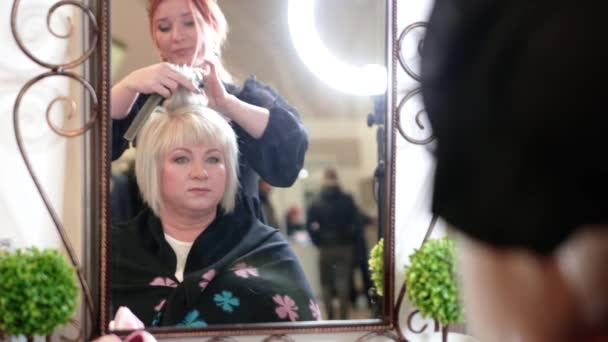 Starsza kobieta z krótkimi siwymi włosami robi stylizację w salonie piękności. Starsza kobieta siedząca przed lustrem. Filmik - Materiał filmowy, wideo