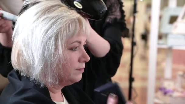 Une femme âgée aux cheveux courts gris fait du coiffage dans un salon de beauté. Femme assise et parlant au téléphone. Vidéo - Séquence, vidéo