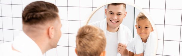 Happy father and son with towels looking at round mirror in bathroom on blurred foreground, banner - Foto, immagini