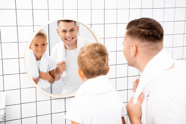 Fröhlicher Blick von Vater und Sohn auf runden Spiegel im Badezimmer im verschwommenen Vordergrund - Foto, Bild
