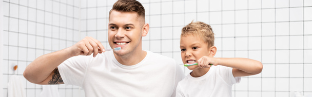 Apa és fia fogat mutat, miközben fogkefét tart a fürdőszobában, banner - Fotó, kép