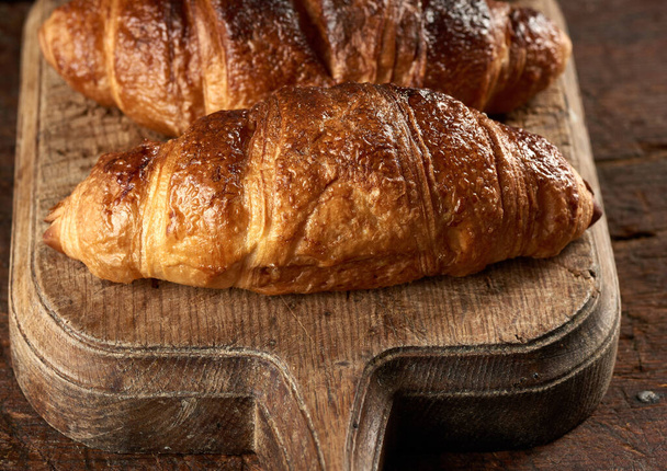 baked croissants on brown kitchen board, black background, close up - Photo, Image