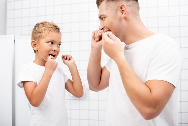 Isä ja poika katselevat toisiaan samalla kun puhdistavat hampaita hammaslangalla kylpyhuoneessa - Valokuva, kuva