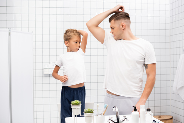 Πατέρας και γιος μυρίζουν μασχάλες ενώ στέκονται κοντά στο νεροχύτη με προϊόντα περιποίησης στο μπάνιο - Φωτογραφία, εικόνα