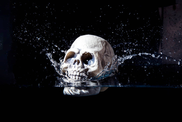 Людський пластиковий череп, що падає у воду ізольовано на чорному тлі
. - Фото, зображення