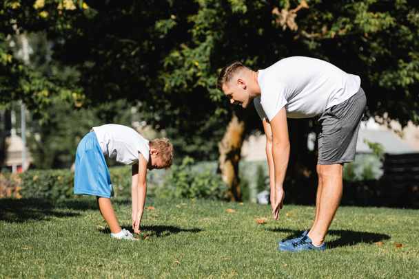 Hombre y niño en ropa deportiva con las manos extendidas, inclinado hacia adelante en el parque con árboles borrosos en el fondo - Foto, imagen