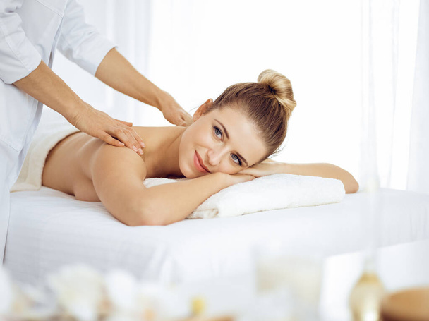 Young and blonde woman enjoying massage of back in spa salon. Beauty concept - Zdjęcie, obraz