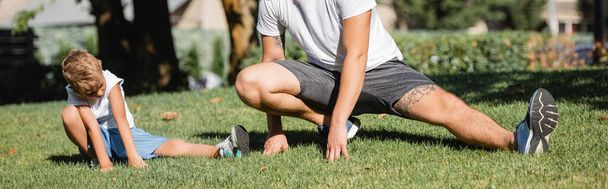 Preschooler boy in sportswear doing lunges near young adult man in park on blurred background, banner - Photo, Image