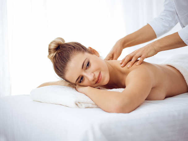 Young and blonde woman enjoying massage of back in spa salon. Beauty concept - Foto, Imagen