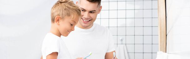 Smiling father looking at son holding toothbrush in bathroom, banner - Valokuva, kuva