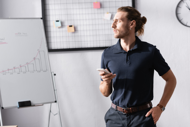 Αυτοπεποίθηση επιχειρηματίας με το χέρι στην τσέπη κοιτάζοντας μακριά, ενώ στέκεται κοντά flipchart στο γραφείο - Φωτογραφία, εικόνα